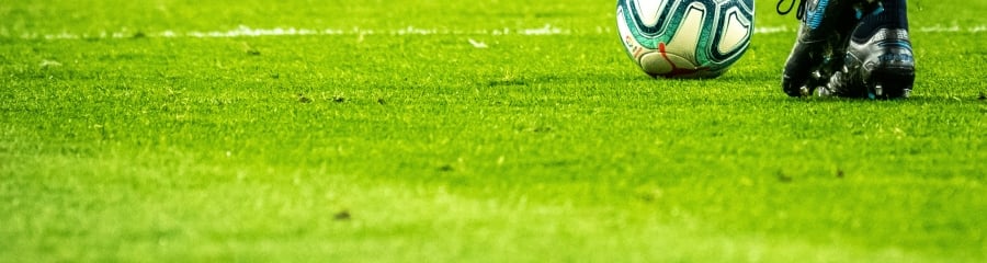 soccer ball near player's cleats on a vivid green field.